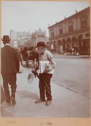 En mann som står på fortauet til Broadway mellom 34th St. og 35th St. og holder avisen The Evening Telegram