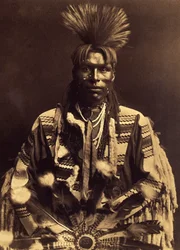 En dandy piegan. Rundt 1855 begynte de unge mennene å skille håret fra den ene tinningen til den andre og krølle ryggen med en stav av en forvarmet rifle. Noen laget nater, andre ikke. Bildet er tatt fra bind 6 av leksikonet publisert