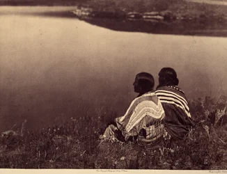 En ledig time - Et øyeblikk av ro: Piegan-indianere som sitter på kanten av en vannmasse. Foto hentet fra bind 6 av leksikonet utgitt av Edward S. Curtis (1868-1952) om indianerne i Nord-Amerika, med et forord av Theodore Roosevelt. B