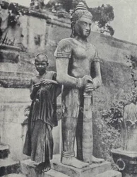 Ung buddhistisk nybegynnermunk ved siden av en statue av Buddha, Fransk Indokina (s/hvitt-bilde)