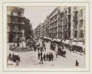Utsikt over Via Roma i Napoli med en statue, butikker, hestevogner og forbipasserende