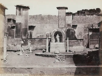 Delvis utsikt over den forhøyede hagen til huset til Marcus Lucretius i Pompeii, dekorert med marmorstatuer og hermer. I midten en fontene med nisje. I bakgrunnen fragmenter av veggmalerier