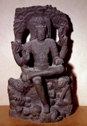 Hinduisme: representasjon av en av Shivas manifestasjoner som sitter på en stein, med fire armer, holder en rosenkrans, ild, i undervisningsgesten og i gave. Skulptur fra 1100-1200-tallet Dim. 1,2 m; Fra Sør-India. C.T Loo Collection