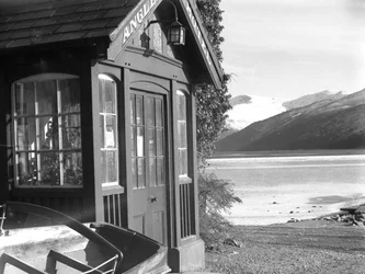 Utsikt over en inngang til «Anglers Hotel», innsjø og fjell til høyre for bildet