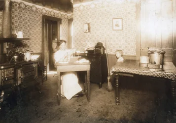 Kvinne setter bust inn i tannbørster på kjøkkenet sitt, ca. 1912