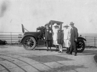 En gruppe mennesker foran bilen sin ved sjøen, ca 1920-tallet