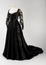 Svart fotsid aftenkjole båret av dronning Alexandra, med perle- og paljettdekorasjon og med dronning Alexandras karakteristiske svarte silkebånd med navn i gullbokstaver, laget av Barolet i Knightsbridge, London, 1908-1910