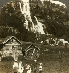 Barn som leker på en bondeåker med terrassert Tvinde-foss, Vossevangen, Norge, c1905.