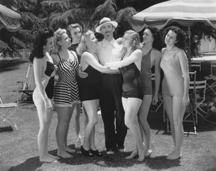 Hollywood, California: ca. 1935 Syv unge kvinner i badedrakter kjemper om oppmerksomheten til en enslig mann. (s/hvitt bilde)