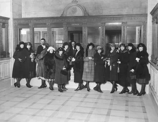 USA: ca. 1926 En gruppe kvinner som står ved «Savings»-kassevinduene i en bank. (s/hvitt bilde)