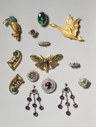 Utvalg av smykker: lysekroneøredobber med ametyst og diamanter; brosje med cabochonslipt stjernesafir og diamanter; ring med svart opal; brosje eller anheng med ametyst og diamanter; gullklipsbrosje med flygende svane; Tiff