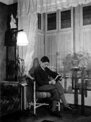 En tenåring som sitter i et borgerlig interiør og leser en bok, har på seg korte bukser og høye sokker. 1915. Historisk foto, kvinne som leser, ca. 1915
