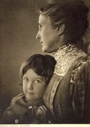 Halvfigurportrett av et barn som ømt omfavnes av en eldre dame. Kvinnen poserer med ansiktet i profil og holder den lille guttens bryst. Han har et livlig og frekt blikk som er rettet mot kameraet.