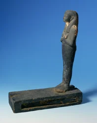 Ptah-Sokar-Osiris-figur med tredelt parykk og kryssede armer på en rektangulær sokkel med et rom som inneholder en del av papyrus (se 83304), egyptisk, 21.-22. dynasti, ca. 900 f.Kr. (tre) (for detaljer se 83306)