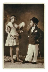 To barn kledd som voksne i 1920-tallsmote. Den lille jenta har på seg et antrekk til Charleston-festen, og han har på seg dress, bowlerhatt og sigarett. Fotografi