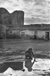 Ung jente leker med en papirbåt i en sølepytt omgitt av gjørme, Venosa, Basilicata, Italia
