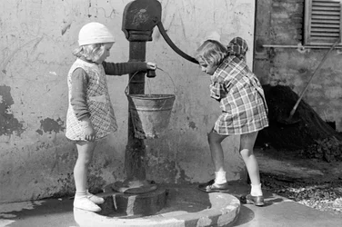 Små jenter fyller en bøtte med vann, 9. mai 1939 (s/h-bilde)