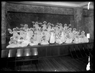 Gruppe med små jenter poserte på en liten scene med fans, sannsynligvis det romersk-katolske orphan asylum, Kingsbridge, Bronx, ca. 1911