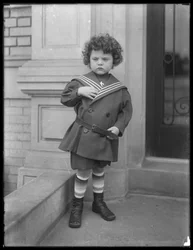 Liten gutt i matrosdress på forkanten av leilighetsbygningen Vermilyea Avenue, ca. 1913