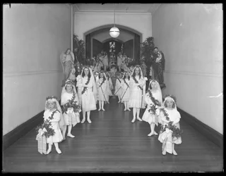 Små jenter på The Roman Catholic Orphan Asylum, Kingsbridge, Bronx, kommer tilbake fra kapellet i hvite kjoler med kranser og kranser, 20. oktober 1914