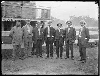 Syv uidentifiserte menn poserer nær en elv eller innsjø, ca. 1910